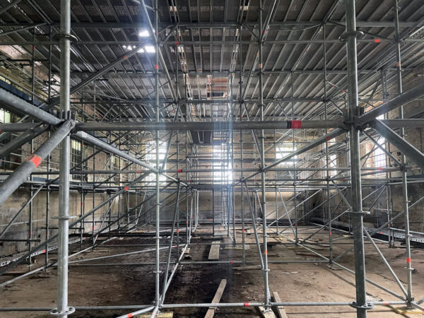 Baustelle zum Rohbaubeginn. Der Raum ist dunkel und ausgefüllt mit Gerüsten.