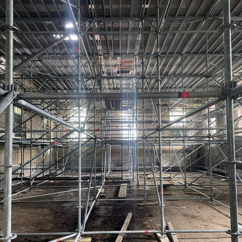 Baustelle zum Rohbaubeginn. Der Raum ist dunkel und ausgefüllt mit Gerüsten.