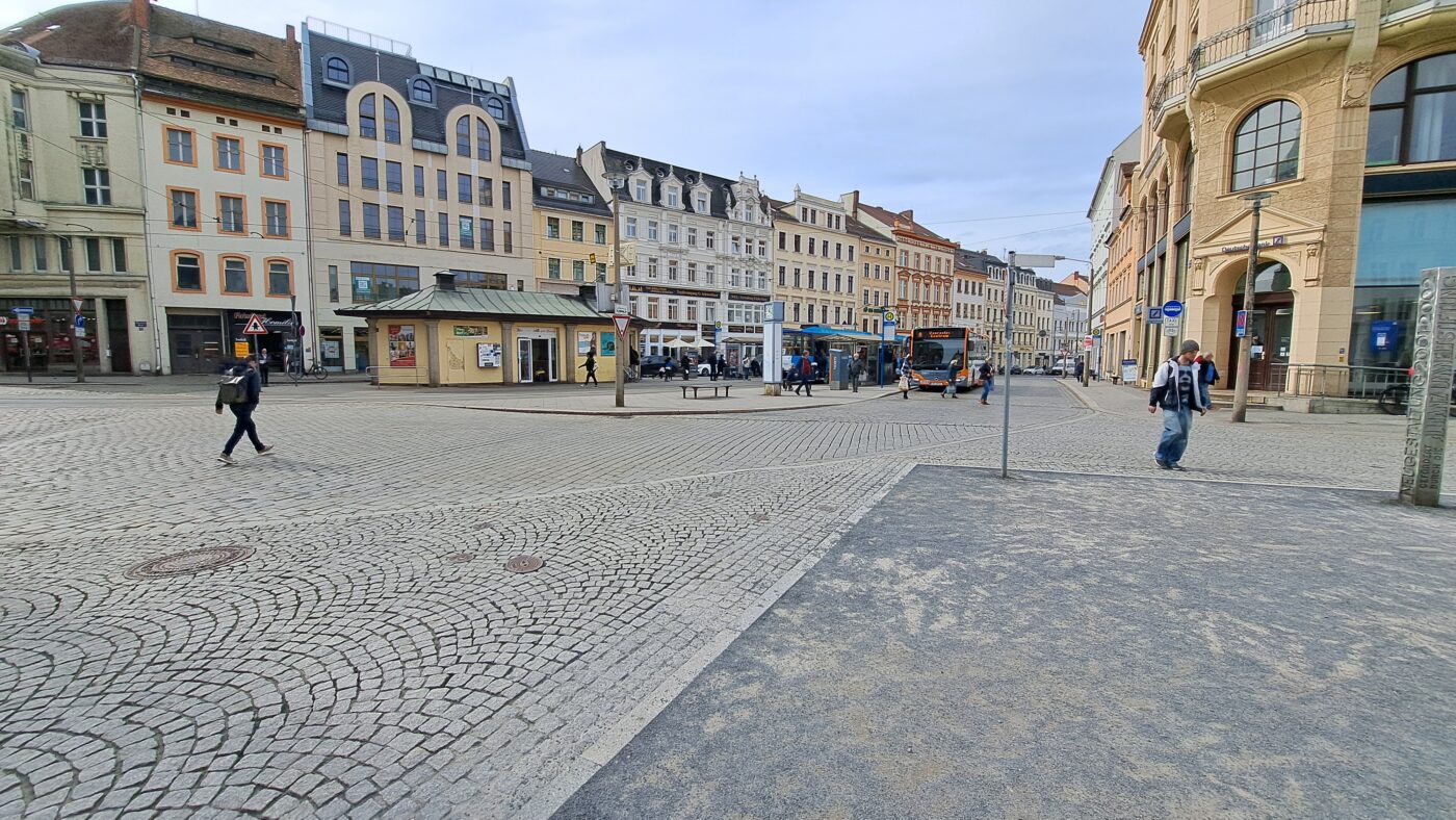 Historische Gebäude bilden einen Platz mit Kopfsteinpflaster. In der Platzmitte ist eine Bushaltestelle