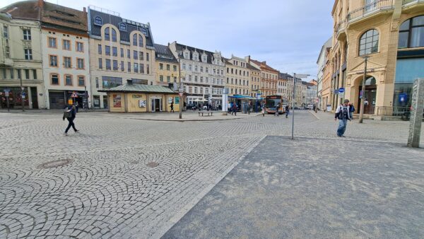 Historische Gebäude bilden einen Platz mit Kopfsteinpflaster. In der Platzmitte ist eine Bushaltestelle