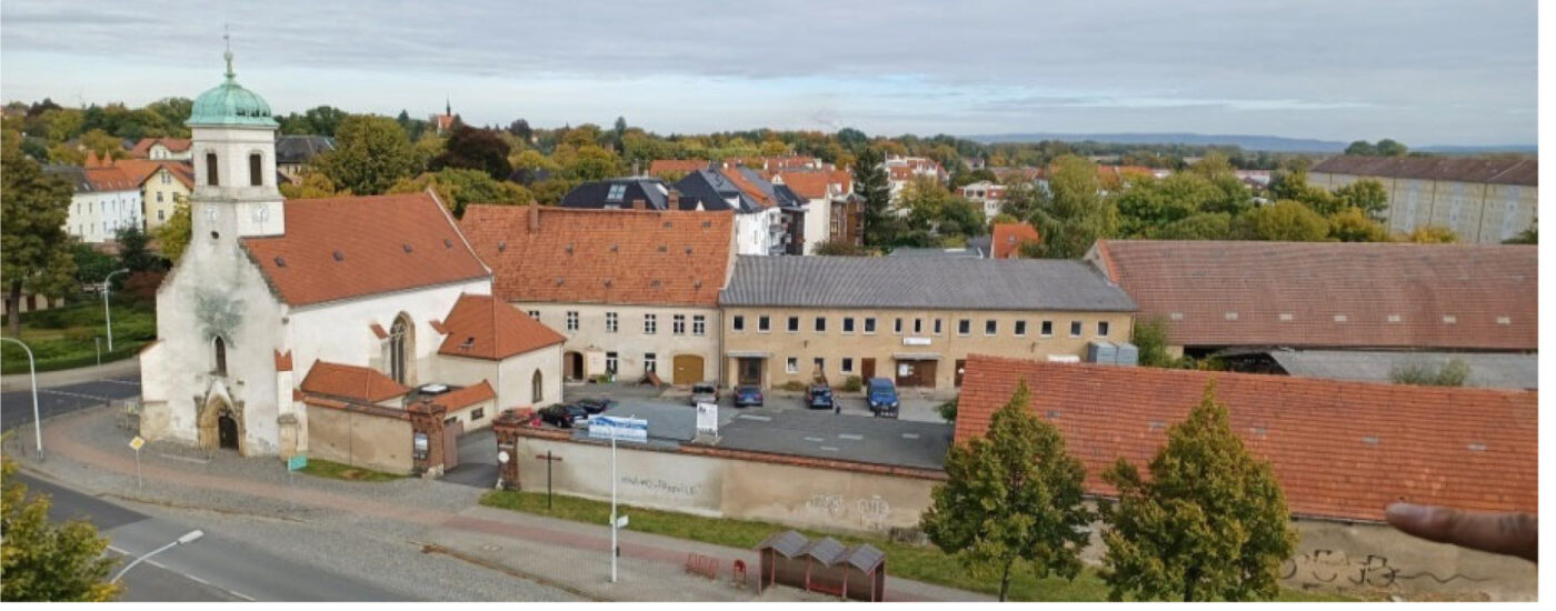 Hof des Hospitalgutes mit Kirche aus der Vogelperspektive. Die städtische Umgebung wird mit gezeigt.