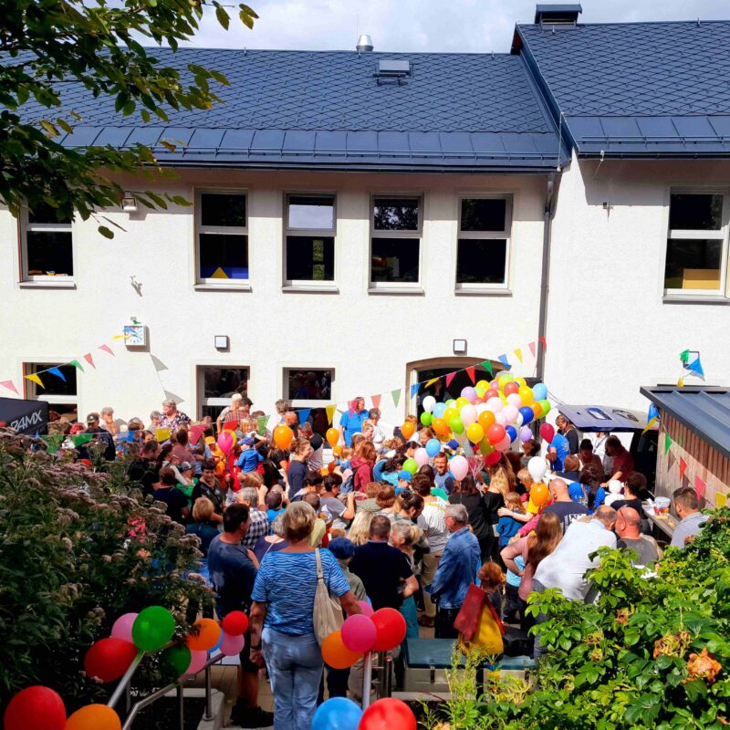 Blick auf Kita mit Kindern und Luftballons
